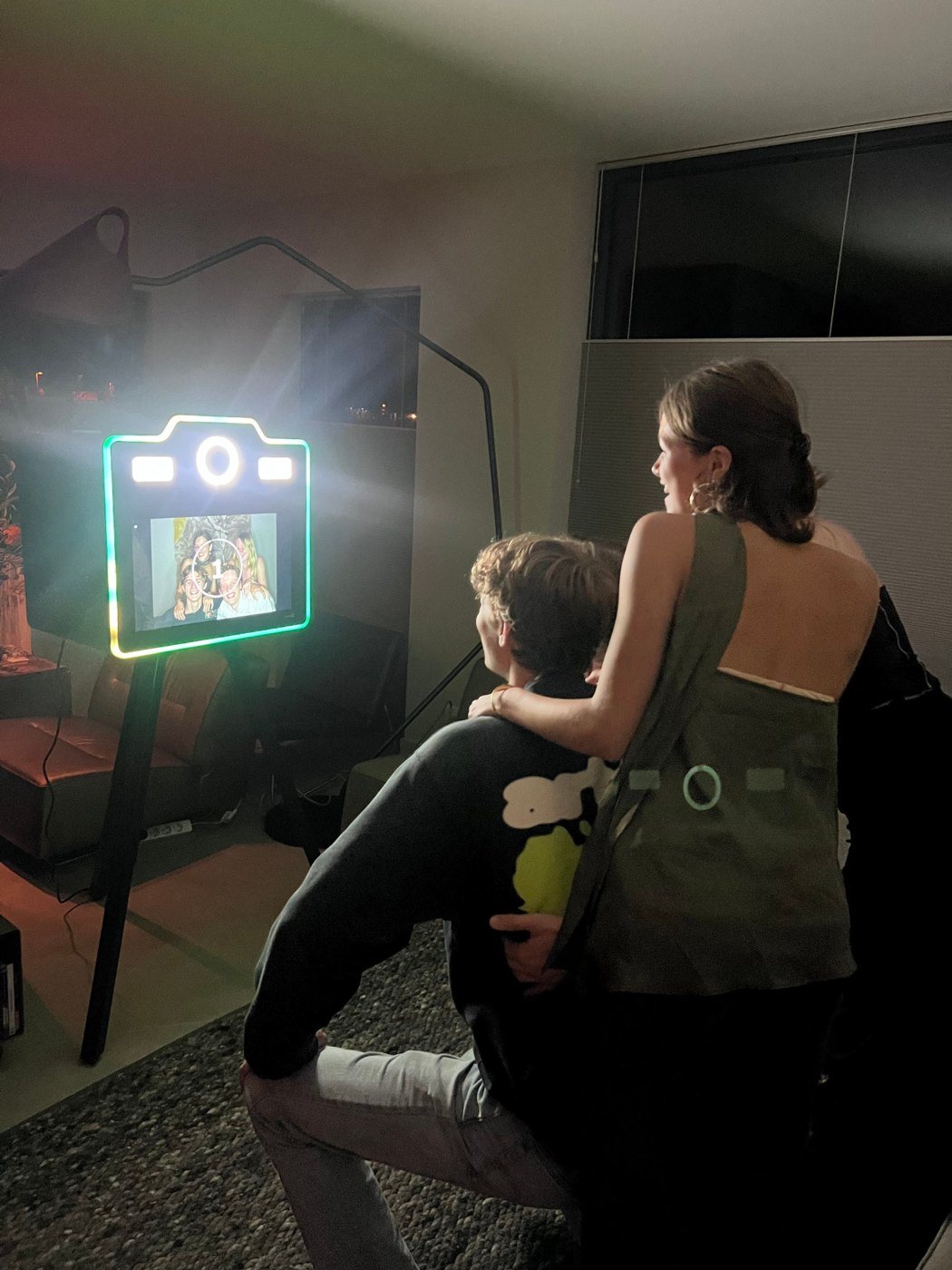 Twee gasten poseren voor de verlichte Posar fotopaal in een donkere woonkamer